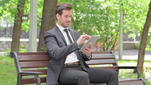 Young Businessman using Tablet while Sitting Outdoor on a Bench