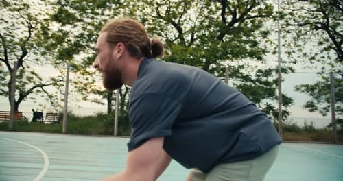 Redhaired Man in a Gray Tshirt Dribbles an Orange Basketball His Opponents Try to Take the Ball Away