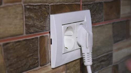 Side view of a man hand plugging and unplugging from the European model wall power socket.