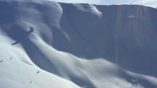 Luftaufnahme, die einen schneebedeckten Berghang hinauffliegt, um eine Bergskyline hinter dem Kamm zu enthüllen.
ich