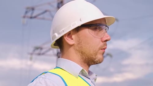 A designer inspects a high voltage tower. An engineer in a hard hat servicing a power transmission p