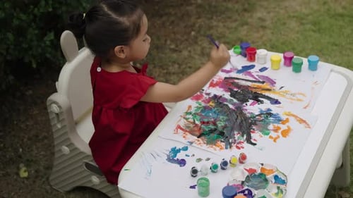 happy toddler girl painting watercolor in a paper at backyard