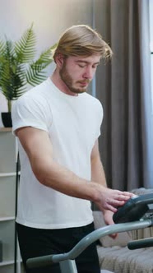 Man in white t-shirt uses treadmill at home