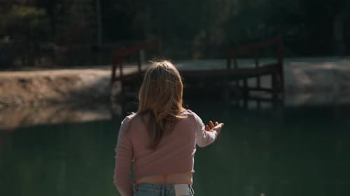 Rear view of young woman throwing rocks into water