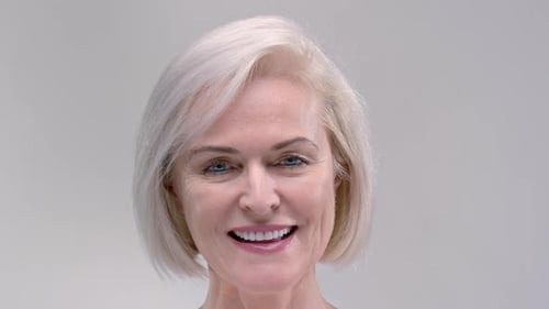 Positive Senior Woman with Short Blonde Hair Smiles Looking Forward on Light Grey Background