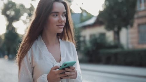 Close Up of Young Beautiful Brunette Girl Using Her Modern Mobile Phone and Looking Around While