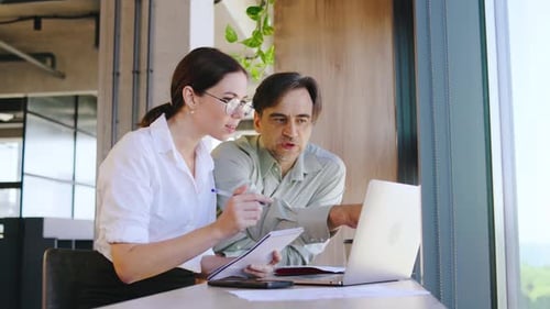 Two Business Professionals Have a Productive Discussion Over a Laptop in a Modern Office Sharing