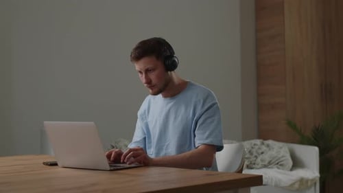 Young Adult Typing at Laptop Wearing Headphones Indoors