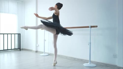 A girl ballet student practices ballet dancing at home with a white background