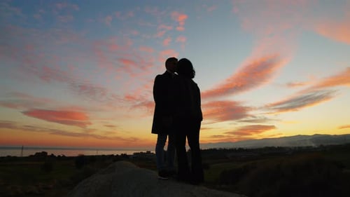 Silhouetted Couple Embracing on Hill at Sunset