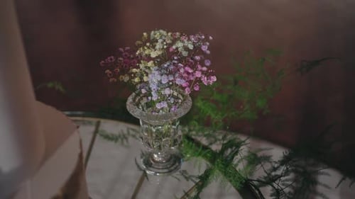 Delicate bouquet of colorful baby's breath flowers in a crystal vase, accompanied by green ferns on