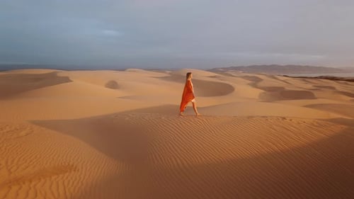 Millennial Young Woman in Orange Dress Walking Barefoot on Scenic Sand Dune