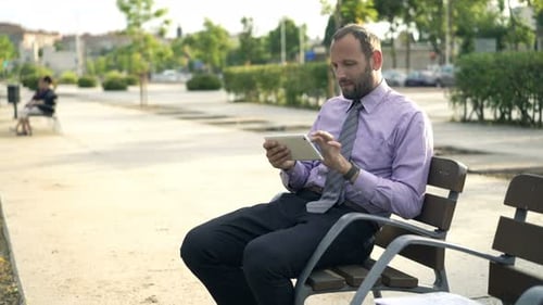 Young businessman browsing internet on tablet while sitting on a bench in the city