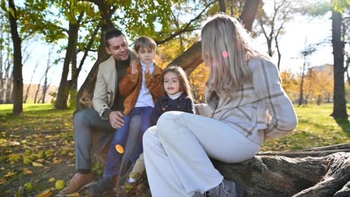 Happy family in an autumn park. Mother, father, son and daughter sitting on a tree trunk, yellowed t