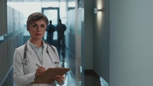 Portrait of Mid-Aged Female Doctor with Clipboard in Hospital Corridor