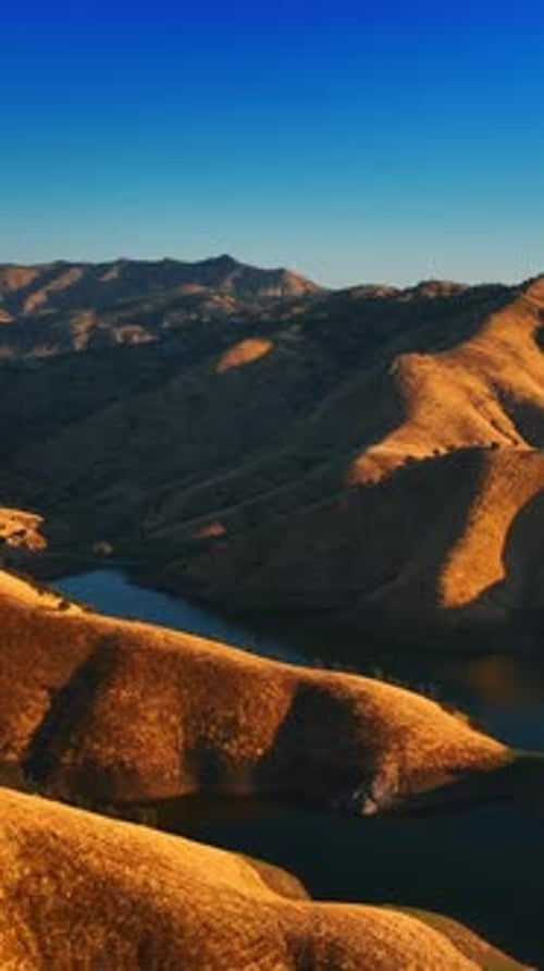 Sunlit Hills and Tranquil River Aerial View