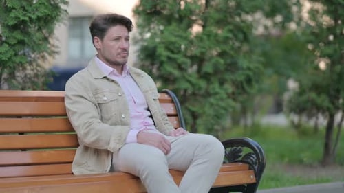 Man Sitting Ponderously on Park Bench in Daylight
