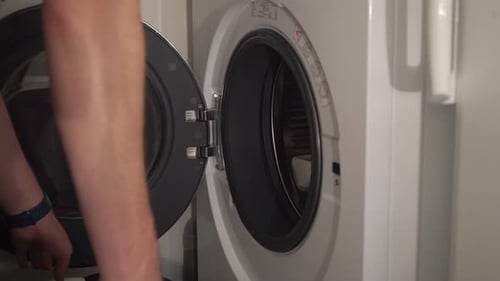 Laundry close-up: Man loads clothes into front load washing machine