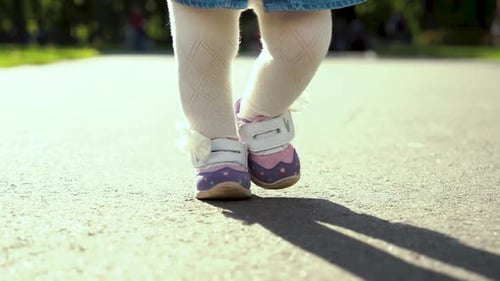 view of stepping feet of toddler girl walking in sunny park with parents