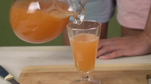Hands of young woman european pours orange juice from a jug into a glass, front side view close up