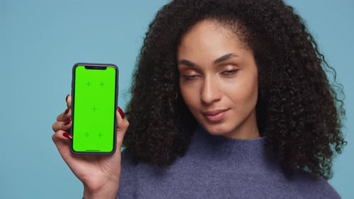 Woman Holding Smartphone with Green Screen Display Against Blue Background