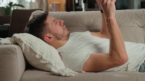 Man Relaxes with Device on Couch at Home