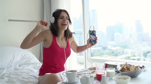 Woman enjoys music while having breakfast in bed