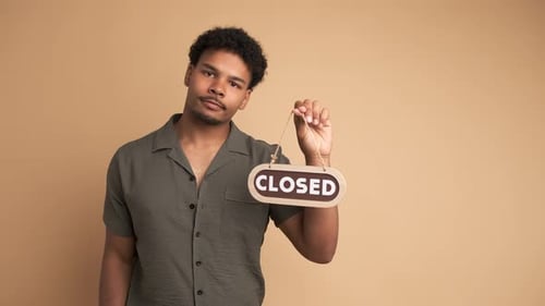 Upset Young Man with Closed Sign in Beige Studio