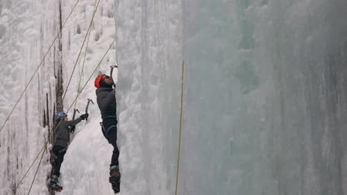 Two ice climbers ascend a vertical ice wall