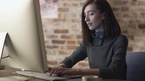 Young brunette woman is working in front of a monitor in a loft.