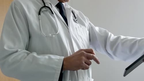 A doctor using a tablet computer in a hospital. The unrecognizable man is standing outside a doctor'