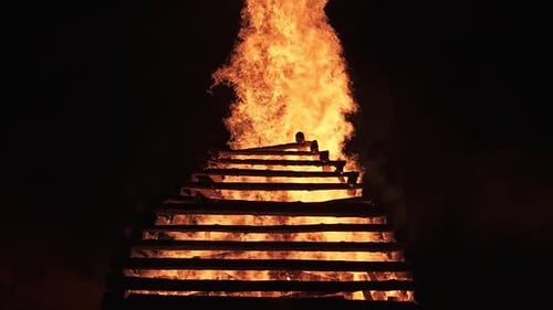 Massive bonfire burning brightly at night with figure silhouette