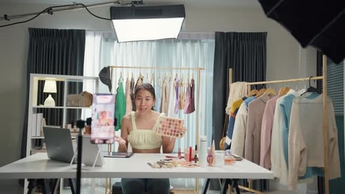 Asia lady blogger look phone camera recording swatch apply eye shadow palette on skin show review.