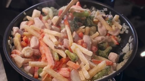 Frozen vegetables added to hot cooking pan with chicken and onions
