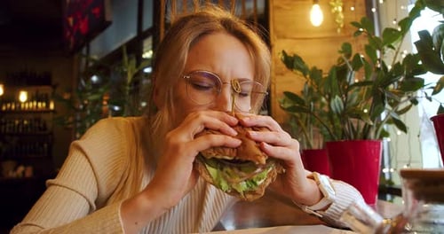 Closeup View of a Young Blonde Woman Eating Fast Food at a Cafe