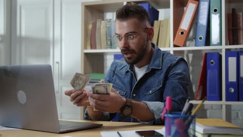 Joven empresario exitoso emocionado que gana dinero en línea y recibe billetes desde una computadora portátil con sorpresa