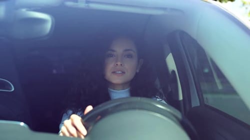 Atraente mulher morena sorridente positiva dentro do carro dirigindo volante giratório olhando