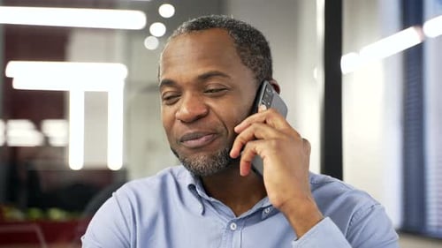 African american businessman talking on mobile phone sitting at workplace in modern office.