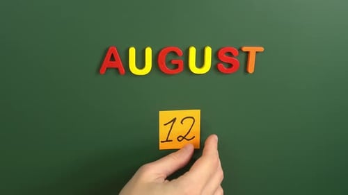Hand sticking a sticker 12 August calendar day on school board. 12 date of august. Twelfth day