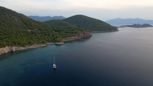 Lone sailing boat on open ocean with island, slow motion rotating drone shot