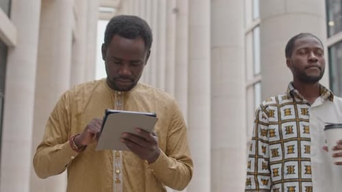 Black Man Using Digital Tablet while Walking along Street in Downtown