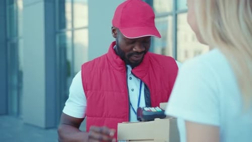 Young African American Delivery Man Hold Package Woman Client Paying By Phone for Parcel