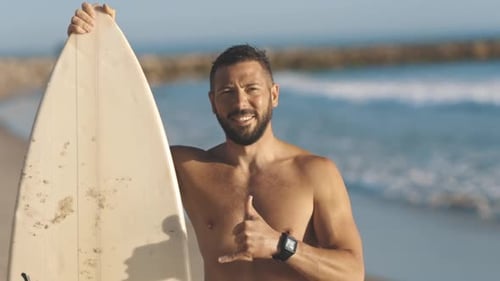 Shirtless Man Holding Surfboard on Sandy Beach