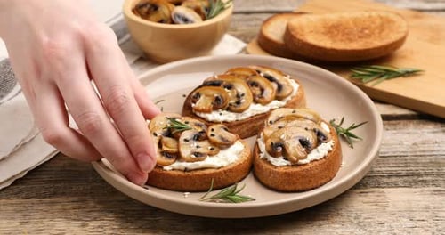 Woman taking tasty bruschetta with cream cheese, mushrooms, rosemary and sesame seeds from plate