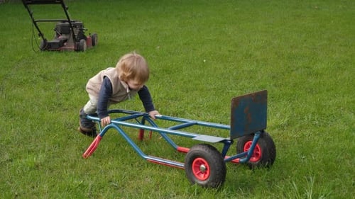 Child Playing on Wheeled Toy in Green Grass