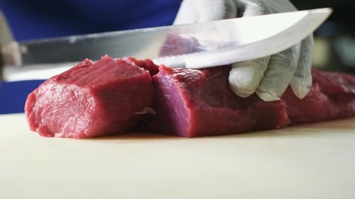 chef in a white gloves and a blue apron in the restaurant kitchen. Preparing food. The cook cuts the