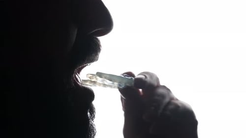 Man putting dental oral alignment retainer on teeth, silhouetted against illuminated white backgroun