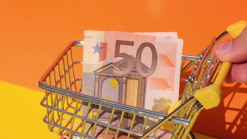 Hand Pushing Toy Supermarket Trolley with 50 Euro Banknote Money in Shopping Cart on Yellow