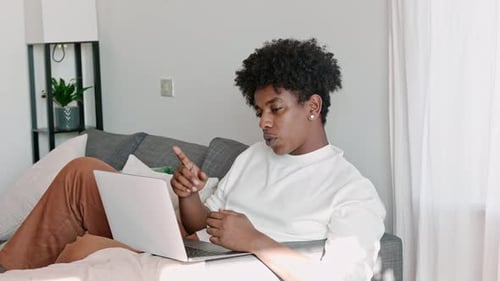 Young Adult Using Laptop on Sofa at Home