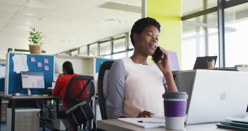 African american businesswoman using laptop and talking on smartphone at office, slow motion